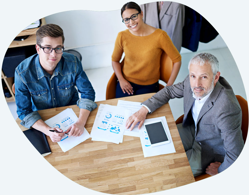 about-1 Older white gentleman in a suit discussing reports with young asian woman and young white man who are both in smart casual outfits.